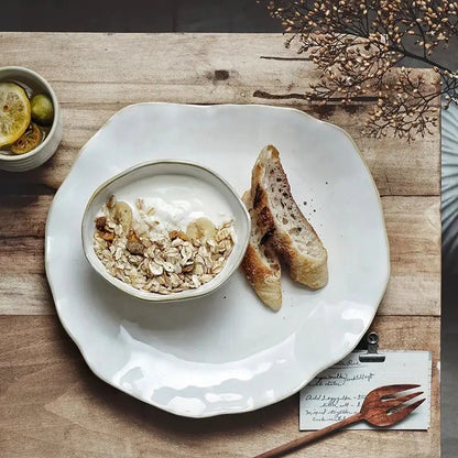 Scalloped white ceramic dinner plate set with a white ceramic bowl filled with yogurt granola and banana slices decorbites ceramic dinner