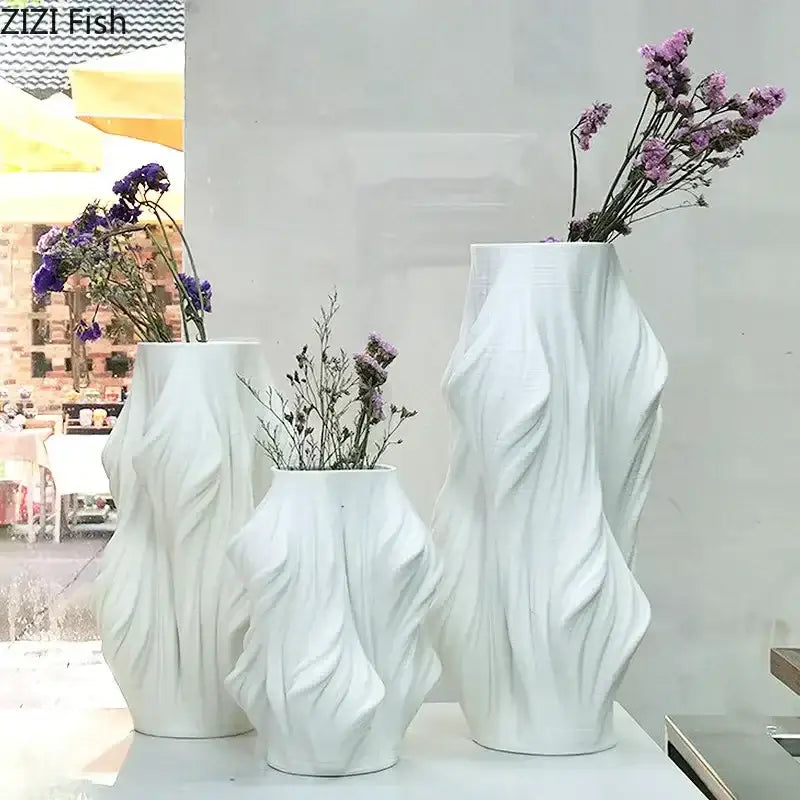 Sculpted white ceramic vase set by decorbites with flowing surfaces holding dried purple flowers for bedroom decor