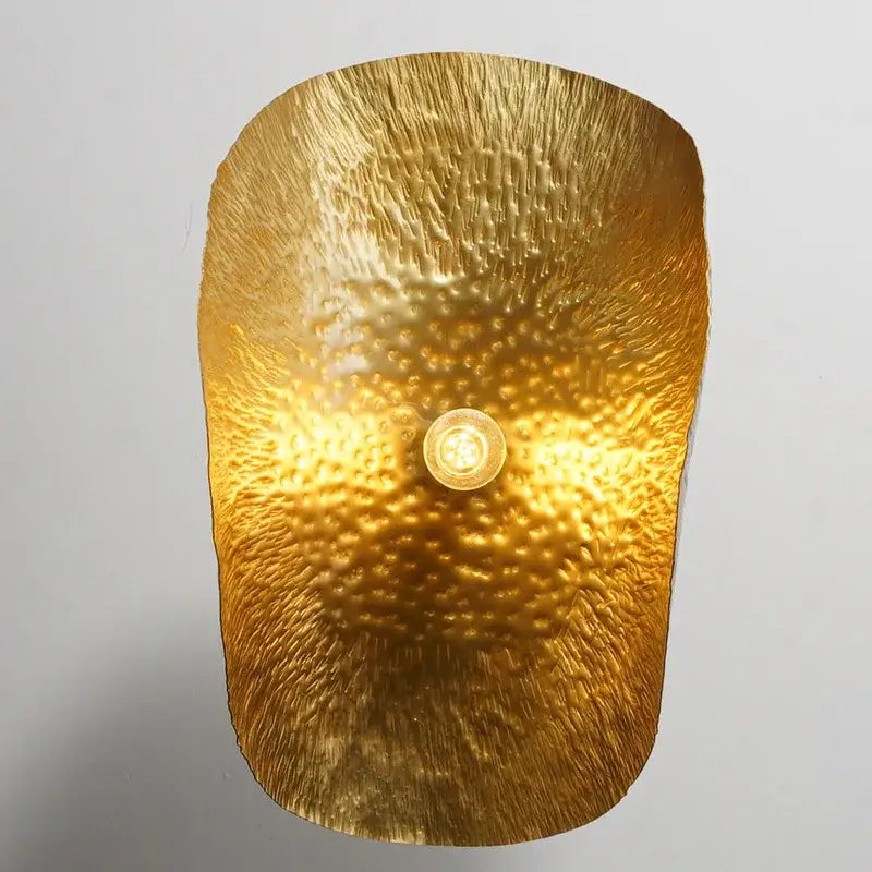 Golden hammered metal wall sconce with textured surface and central bulb from decorbites brass lotus leaf chandelier collection