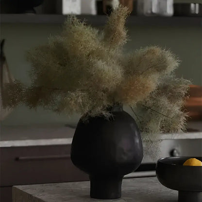 Black matte ceramic vase with dried feathery grasses featuring a sculptural white hammer pattern for living room desk