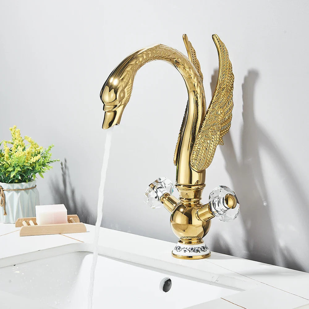Golden swan-shaped deck mounted bathroom faucet with cold water crystal knobs and ornate wing detailing in brass