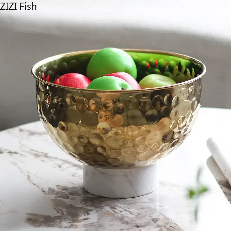 Gold-toned hammered metal fruits bowl with white marble pedestal base featuring a hammer pattern design