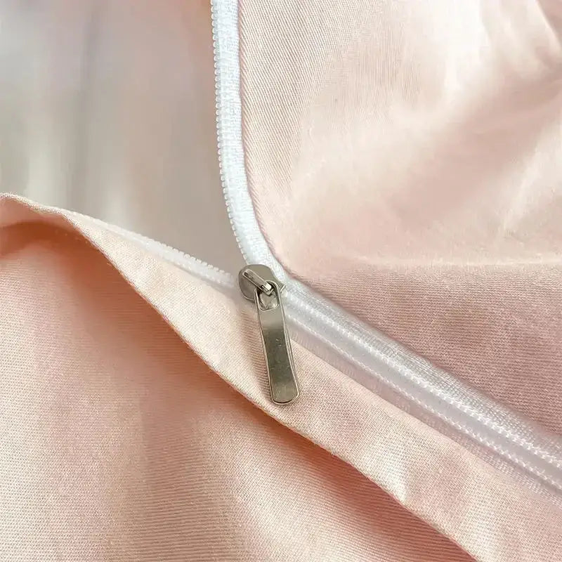 A sleek silver zipper with a metallic pull tab on blush-pink satin fabric of a decorbites cotton king size bedding set