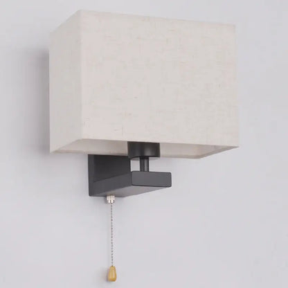 A modern black metal light fixture with an off-white fabric rectangle shade and wooden pull chain for bedroom use