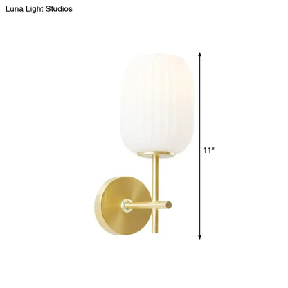 Gold-finished wall sconce light fixture with a vertically ribbed cream glass shade for bedroom use