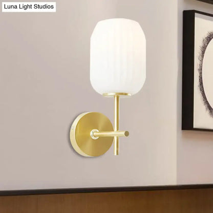 Gold-toned bedroom wall sconce light fixture with cream glass shade and vertically ribbed frosted glass design