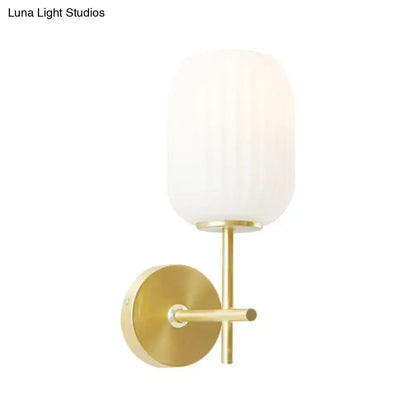 Gold-toned bedroom wall sconce light fixture with cream glass shade and frosted vertically ribbed glass design