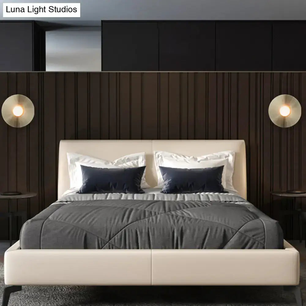 Cream upholstered bed with dark navy pillows paired with simplicity brushed brass circular wall light fixture bedroom sconce