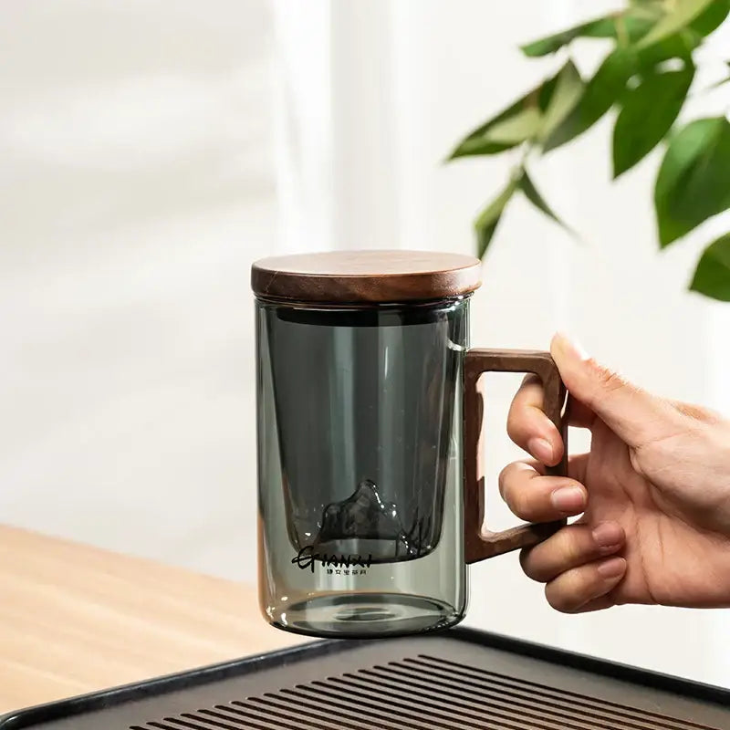 A sleek dark gray double walled glass tea cup with wooden lid and handle perfect for kitchen use