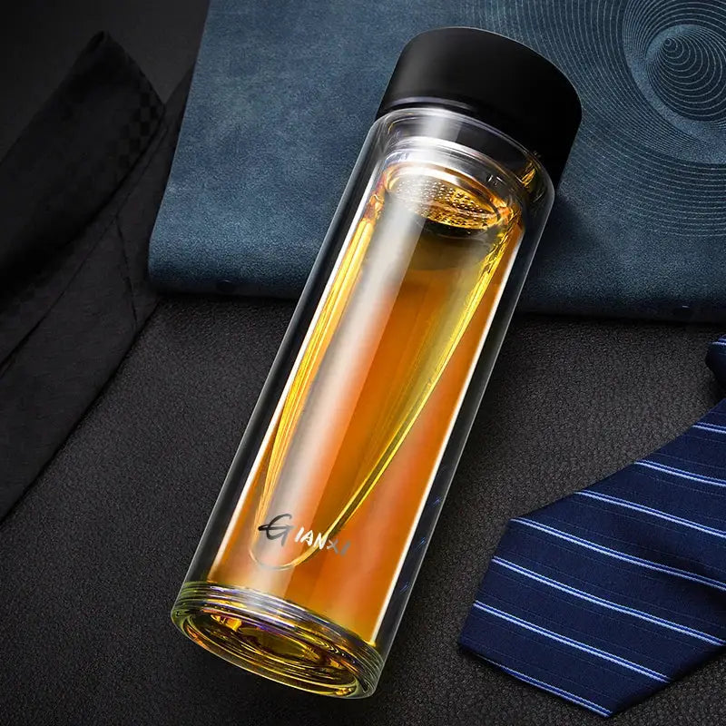 Sleek clear double-walled glass water bottle with black lid filled with amber liquid and built-in filter