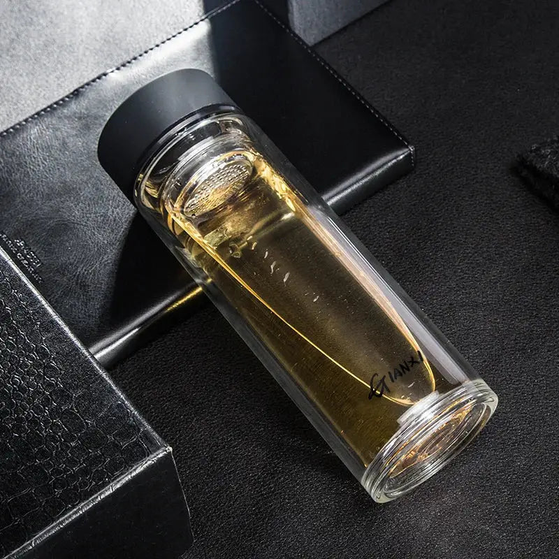 Sleek clear double-walled glass water bottle with black lid filled with golden liquid for kitchen use