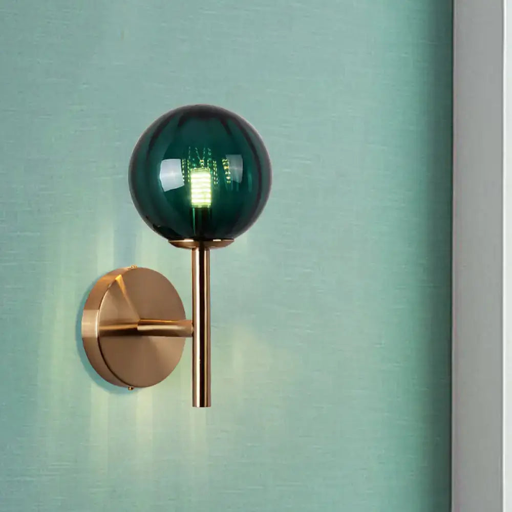 A sleek brass bedside sconce light with round wall lighting featuring a spherical emerald green glass globe in red green amber