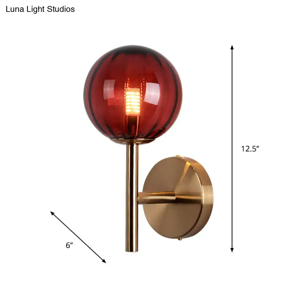 A sleek brass round wall lighting with a deep red glass globe and filament bulb bedside sconce light