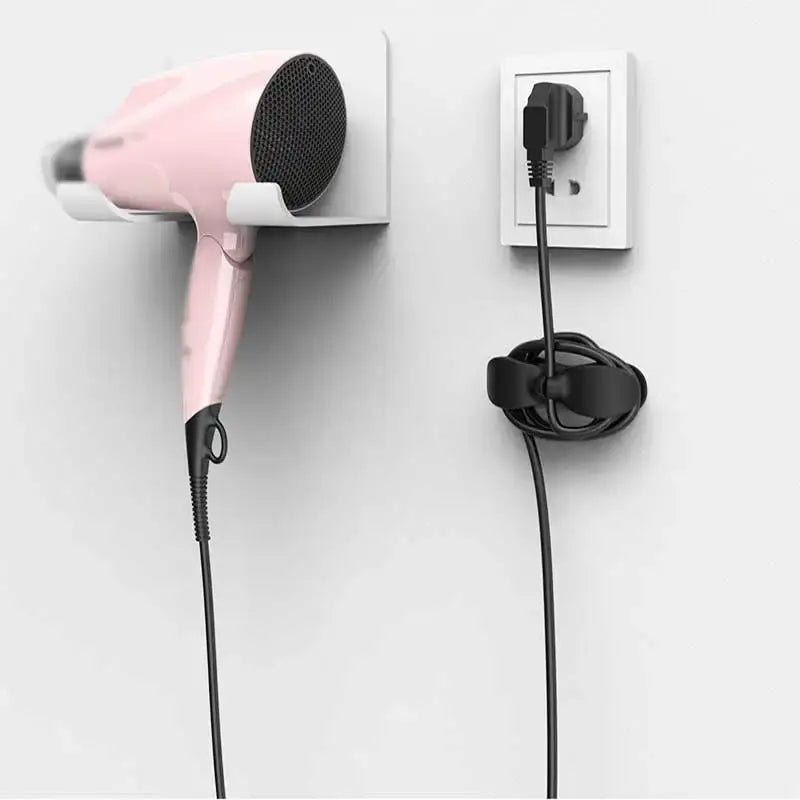 Pink hair dryer with black mesh grille and handle mounted on white wall holder next to sleek silicone decorbites cord winder cable organizer