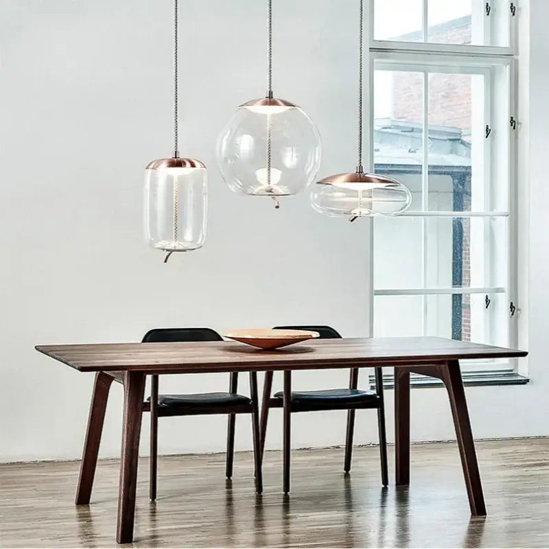 Three modern glass led chandelier pendant lights with copper tops hang above a wooden dining table in living room