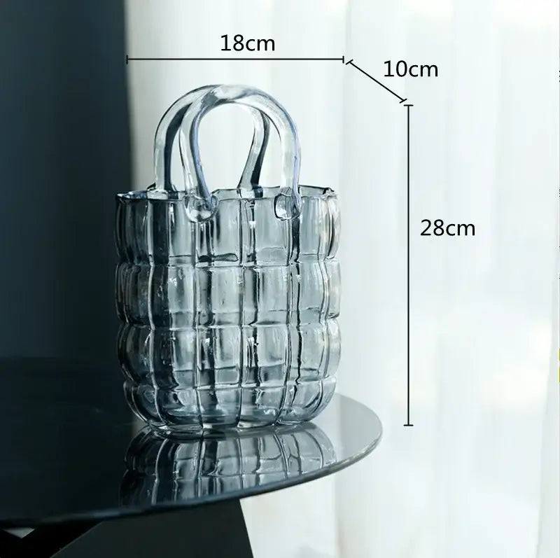 Smoky gray and amber clear glass vase beside a transparent glass tote bag with geometric quilted design and clear handles