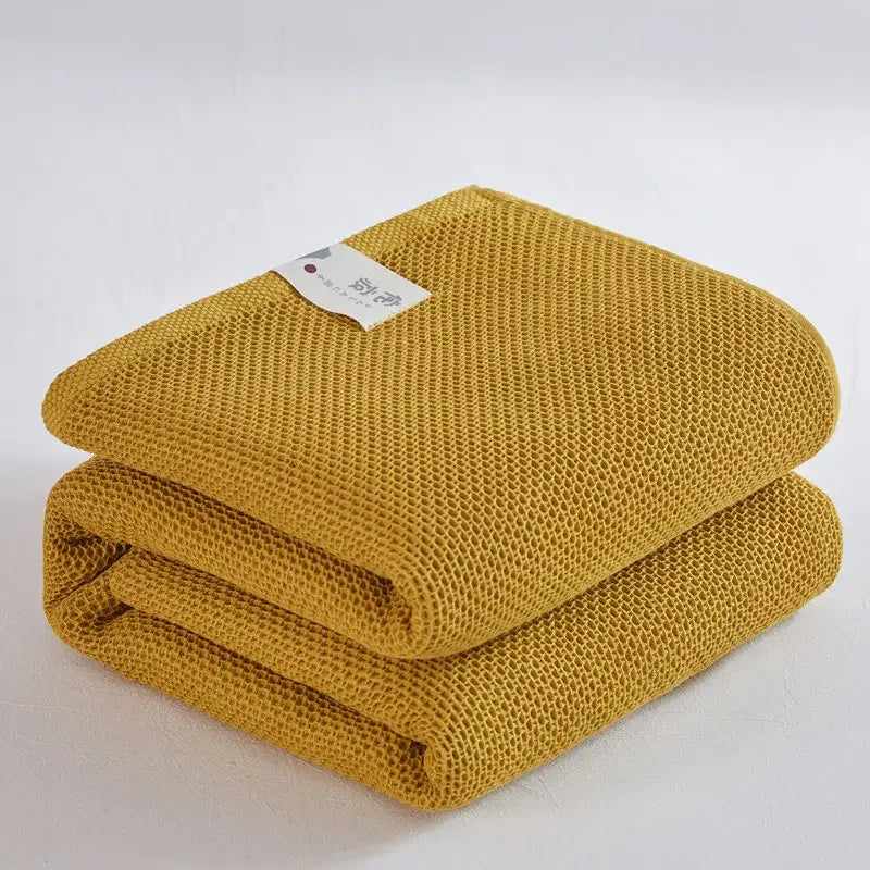 A neatly folded mustard yellow cotton honeycomb towel blanket by decorbites for living room couch decor