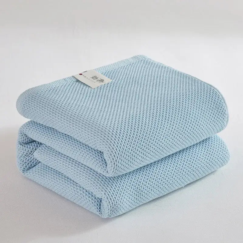 A soft light blue cotton honeycomb towel blanket with textured mesh pattern and neatly folded edges for living room decorbites