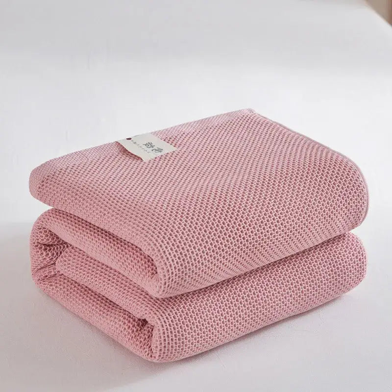 A soft pink cotton honeycomb towel blanket folded neatly with a white label ideal for living room couch decorbites