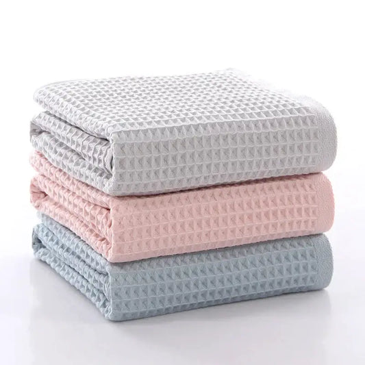 Stack of three folded decorbites cotton waffle towels in soft gray blush pink and muted blue for bathroom use