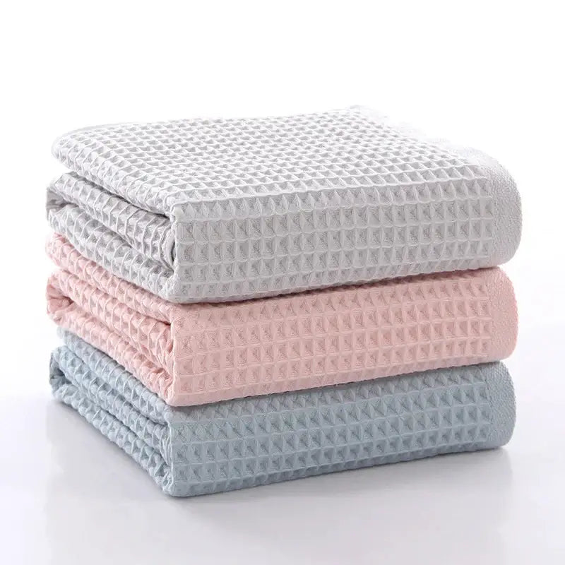 Stack of three folded decorbites cotton waffle towels in soft gray blush pink and muted blue for bathroom use
