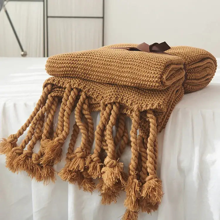 A cozy mustard-yellow decorbites knit throw blanket with thick rope tassels and brown ribbon tie for bedroom decor