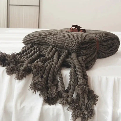 A cozy dark gray decorbites knit throw blanket with thick braided tassels and a brown ribbon tie for living room decor