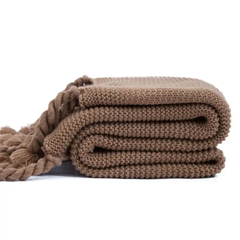 A neatly folded taupe decorbites knit throw blanket with ribbed texture and braided tassels for soft plaid decor