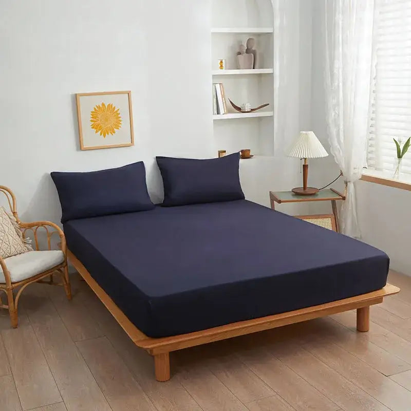 Navy blue decorbites cotton fitted sheet with matching pillowcases on wooden bed frame in soft yellow and beige bedroom decor