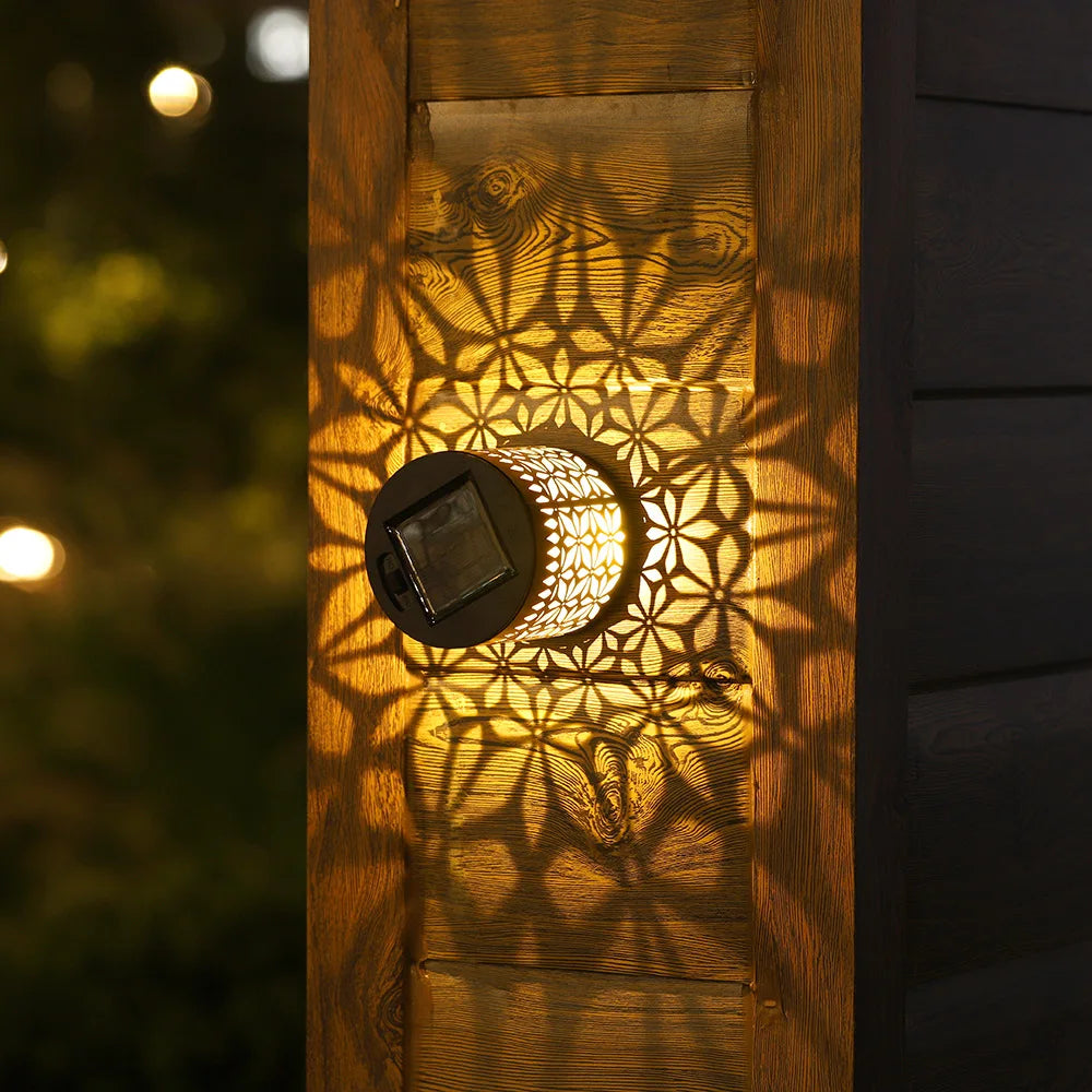 Solar-powered datura lantern light with black base and floral cut-outs casting shadows on wooden outdoor surface