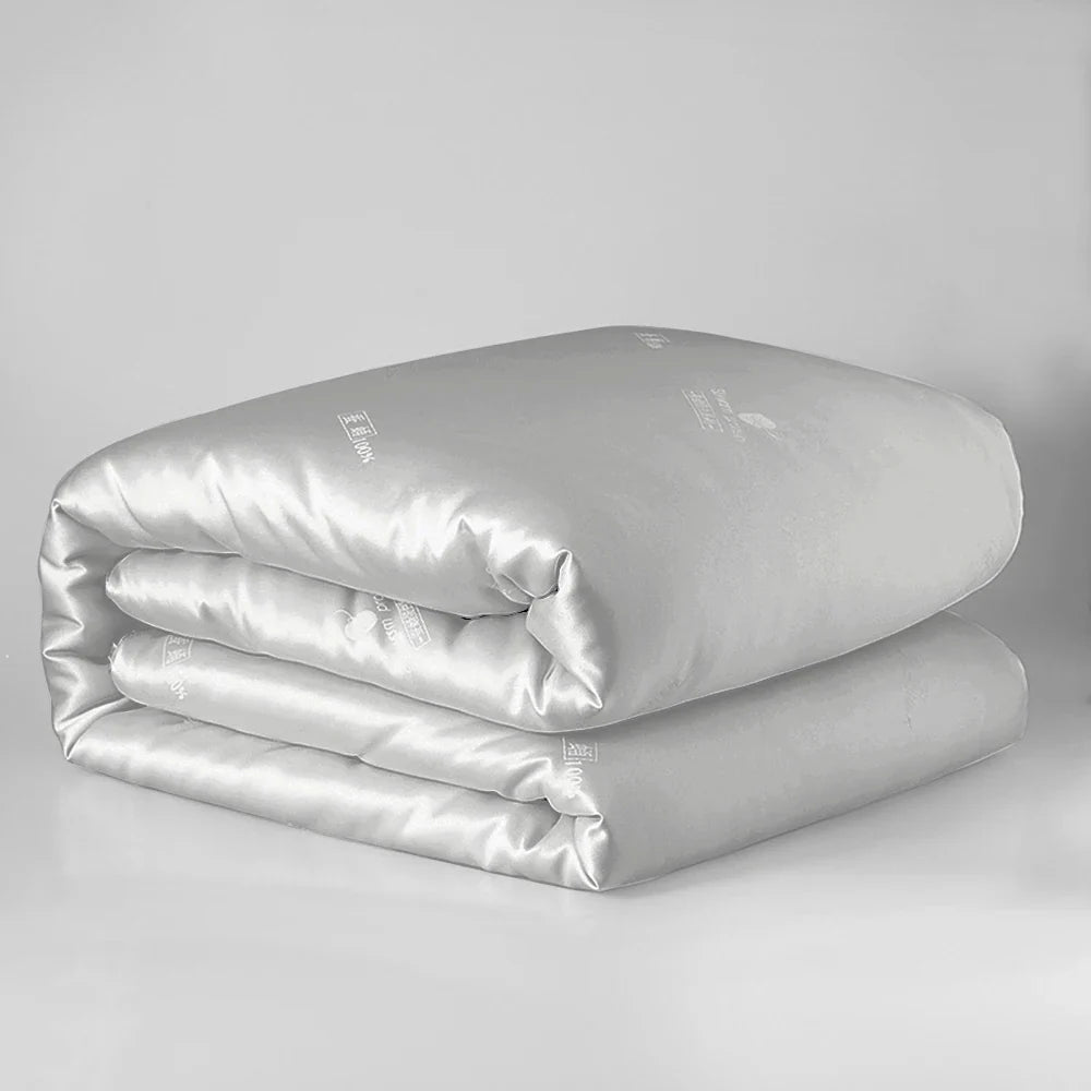 A sleek silver satin-finish sondeson luxury natural 100% silk quilt with subtle embroidered branding for sleep comfort