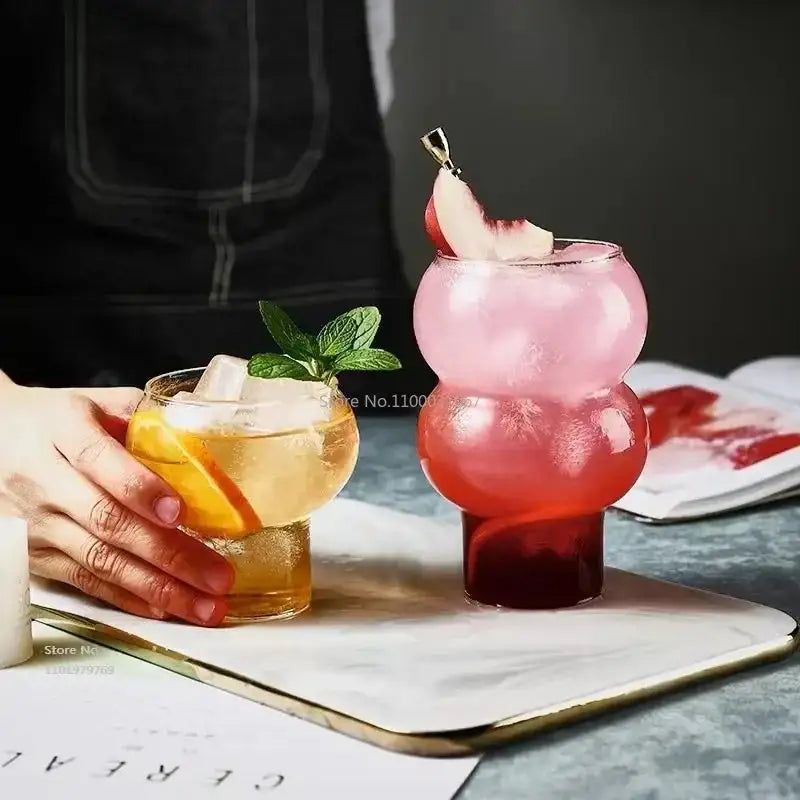 A vibrant two-toned stacked ribbed glass cold brew coffee cup with a playful bulbous design holding a pink and red drink