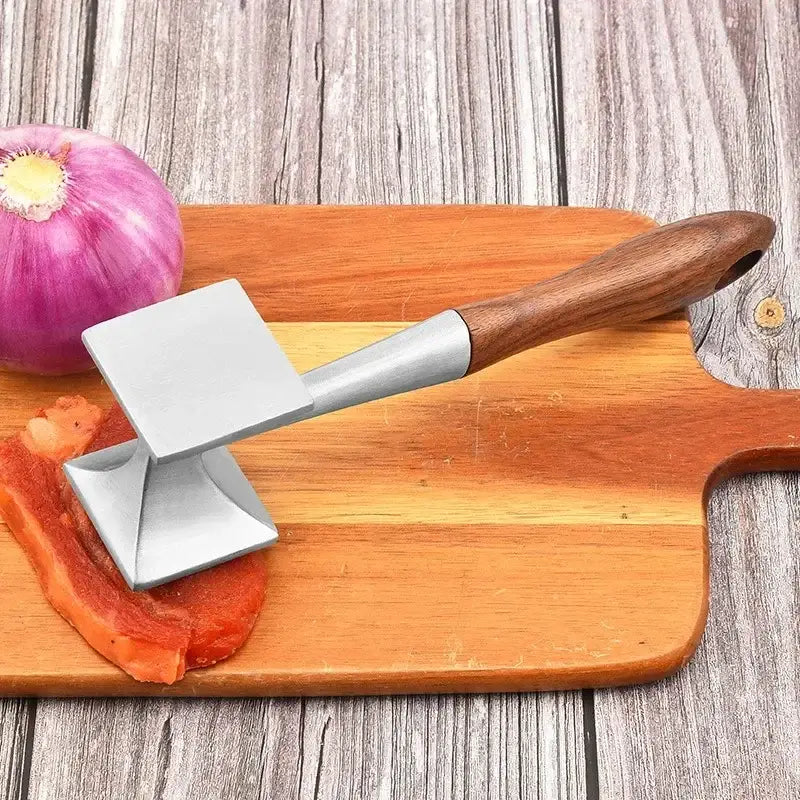 A stainless steel meat tenderizer with a polished wooden handle rests on a wooden cutting board