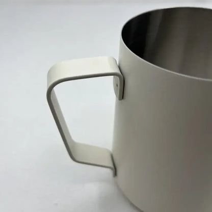 Cream-colored stainless steel milk frothing jug with measurements and minimalist modern design for milk frothing use