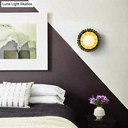 A modern sunflower yellow wood wall sconce with matte white glass ball and dark brown petal-like outer rings for bedroom