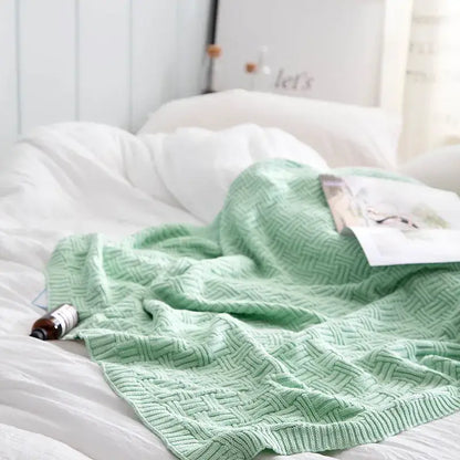 A soft mint green cozy jacquard blanket with textured herringbone pattern draped over white bedding by decorbites