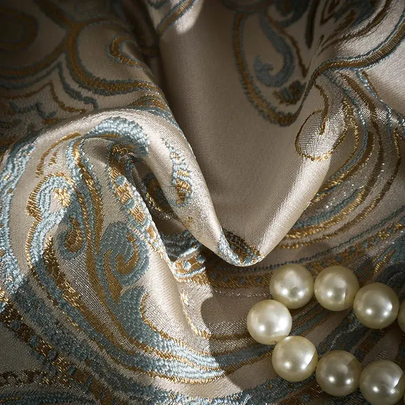 Beige silk fabric with intricate teal and gold paisley embroidery and cream pearls on a 200s egyptian cotton bedding set
