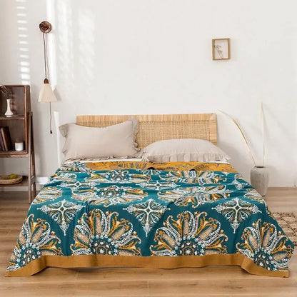 Teal and gold paisley decorbites bohemia cotton blanket displayed with a woven rattan headboard in the background