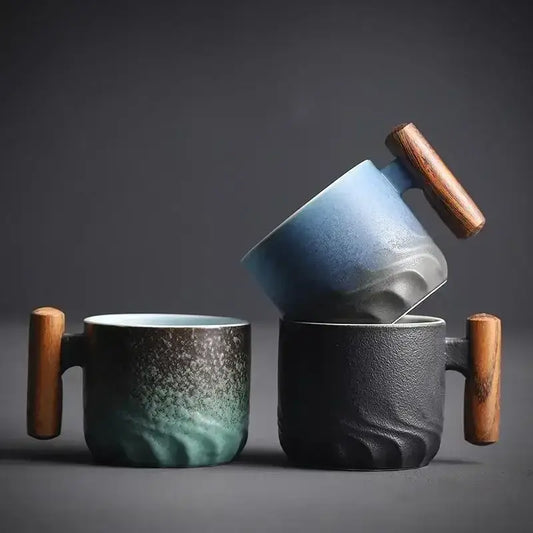 Two ceramic coffee cups with wooden handles featuring a teal gradient glaze and textured black finish for kitchen use