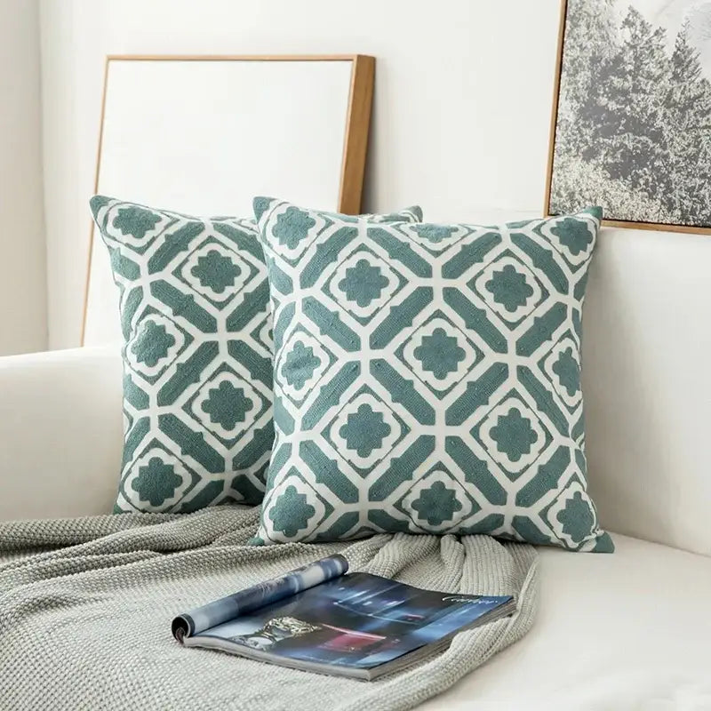 Two teal and white embroidered geometric floral cushion covers with textured fabric for living room decor