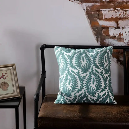 Teal and white blue geometric embroidered cushion cover with leafy damask design resting on dark brown leather bench decorbites