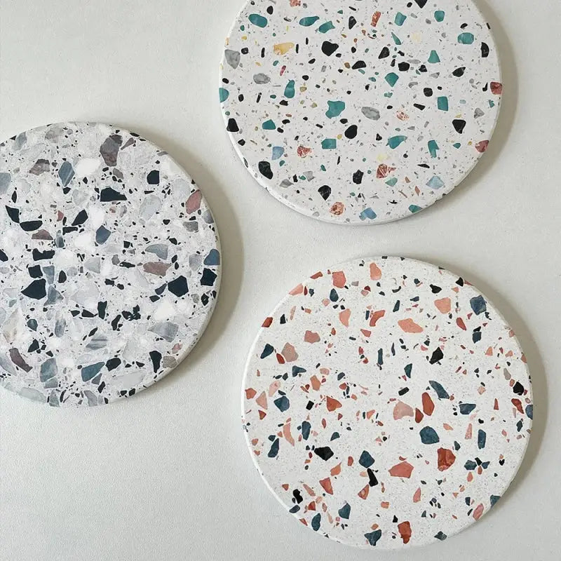 Three circular decorbites diatomite coasters with terrazzo pattern in white black gray teal and muted pink tones for dining use