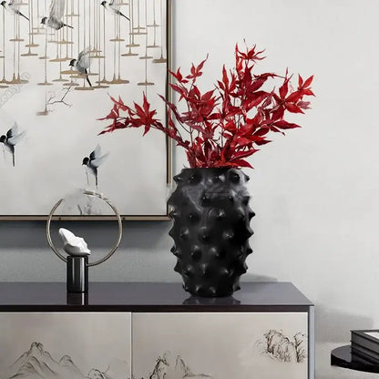Textured black ceramic flower vase with spiky surface holding red artificial maple leaves for decorbites black ceramic decor
