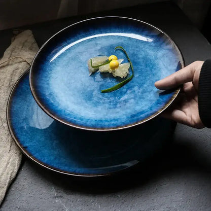 A hand holds a deep blue textured ceramic dinner plate with gradient glaze and dark brown rim from decorbites dinner plate set