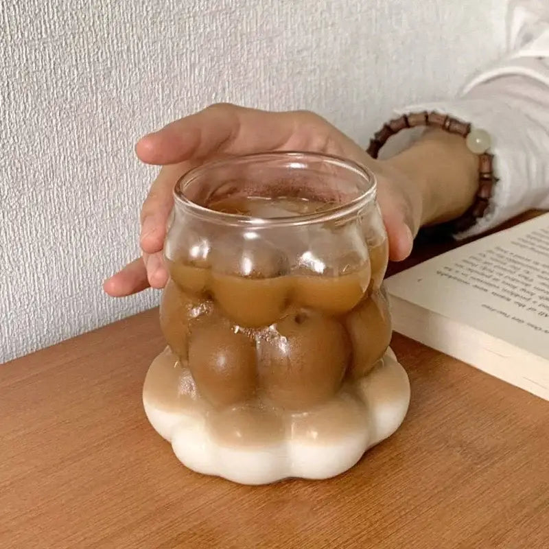 A clear glass tumbler with a rounded flower-like shape and white base from a textured glass drinking set
