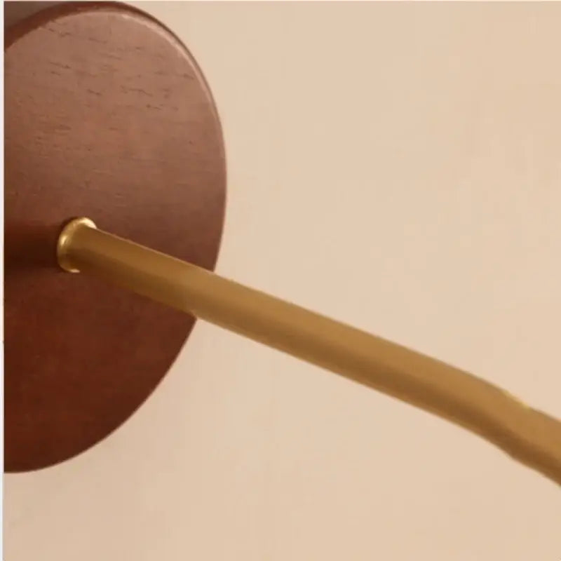A sleek brass rod extends from a circular rich brown wooden wall plate on decorbites adjustable led wall light