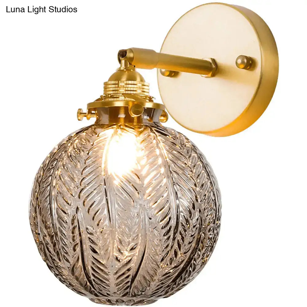 Brass-finished bedroom wall sconce with a textured glass ball featuring a frosted globe with an intricate leaf pattern