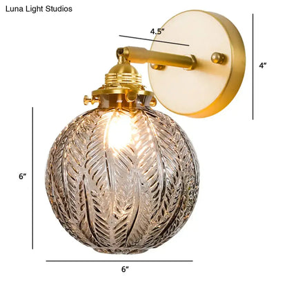 Gold-finished bedroom sconce with textured glass ball globe featuring etched leaf-like patterns for wall lighting