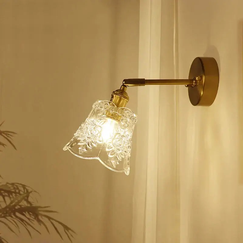 A clear glass lampshade with floral etchings mounted on a brass mirror wall sconce for bedroom decorbites brass mirror