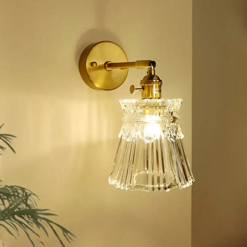 Brass-finished wall sconce with textured clear glass shade and scalloped edges for bedroom decor by decorbites brass mirror